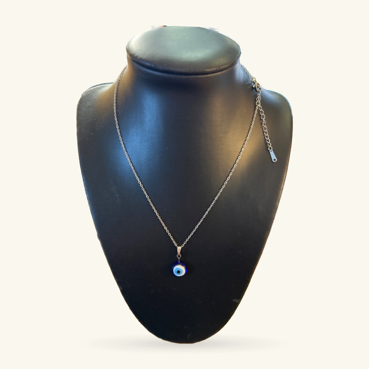 Evil eye necklace with small blue and white pendant on silver chain, displayed on black bust
