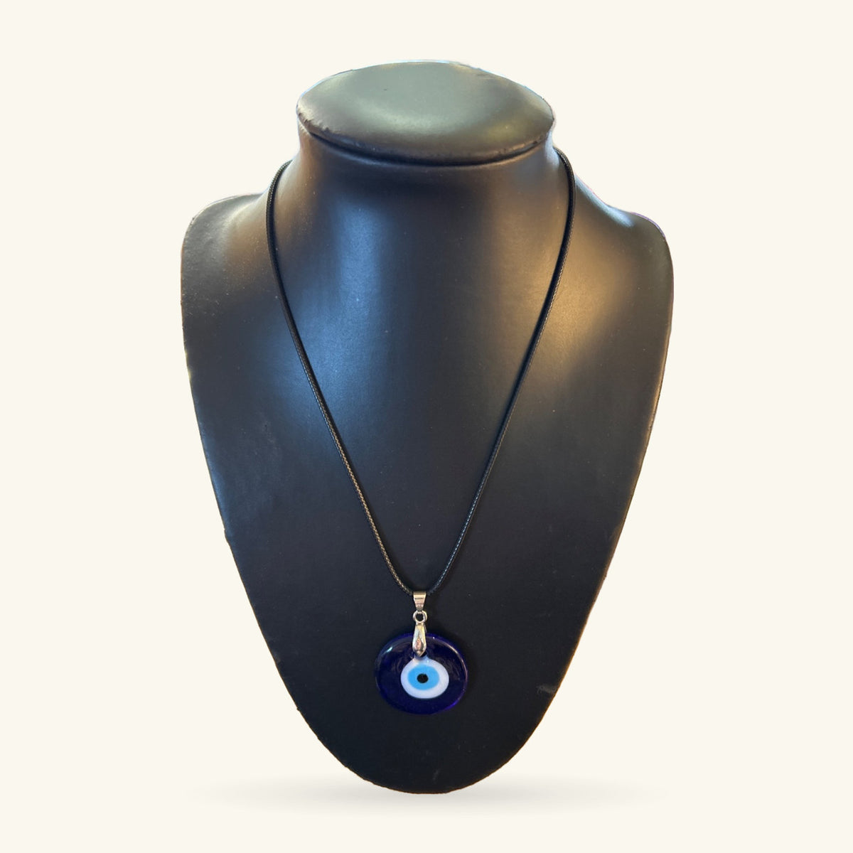 Evil eye necklace with dark blue circular pendant on black cord displayed on a black bust form.