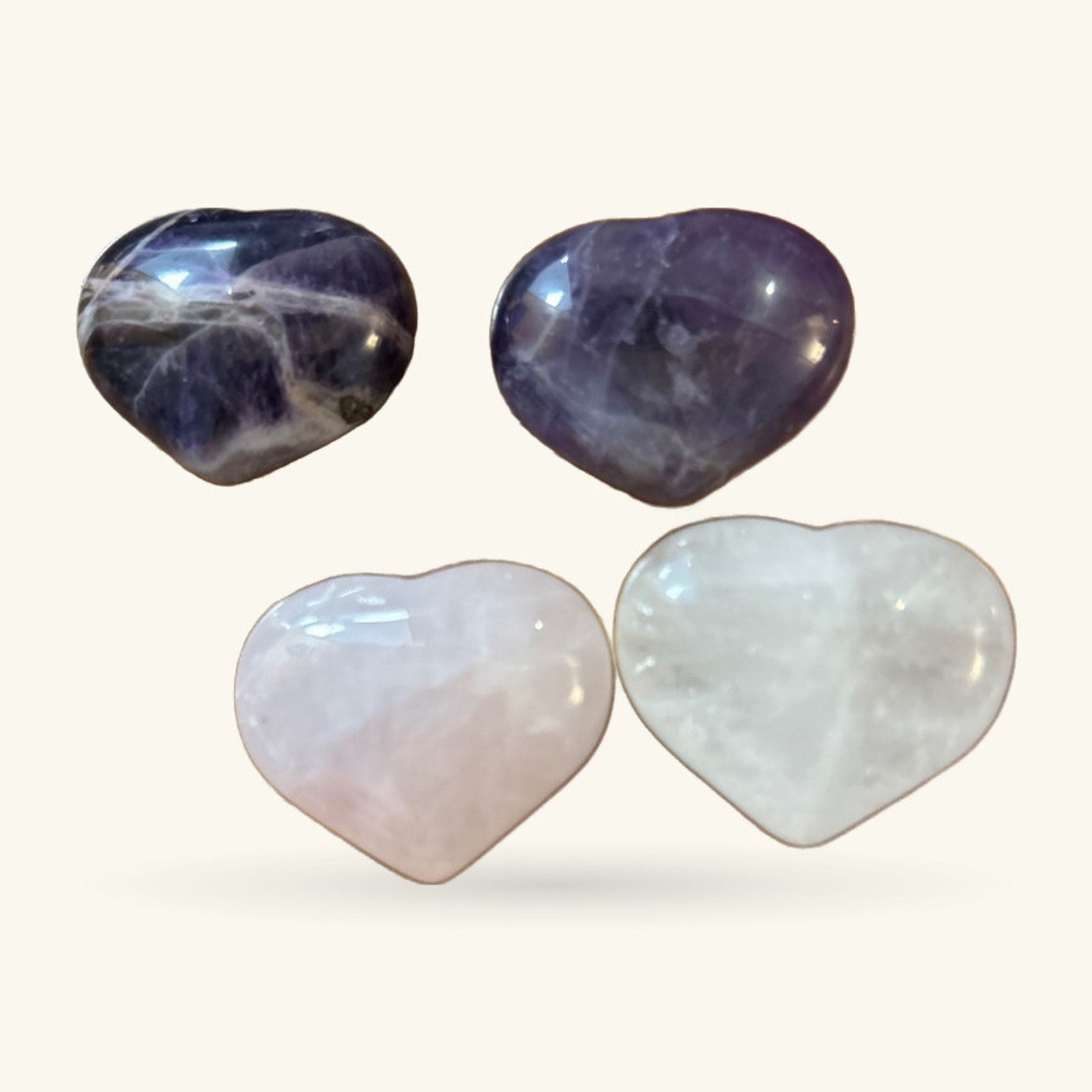 Four polished crystal hearts: two dark purple amethyst stones on top, two pale pink and white quartz stones below.