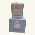 A pale blue cylindrical candle with decorative house illustration and 'A happy home' text, shown with its lavender box