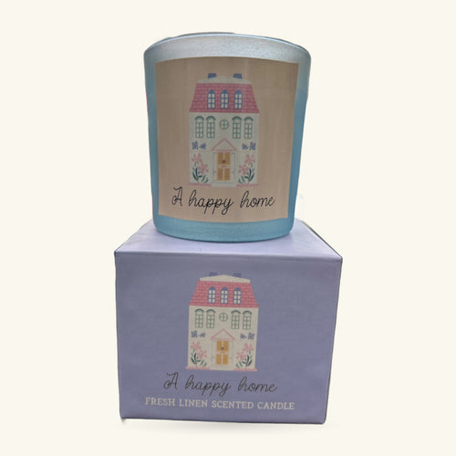 A pale blue cylindrical candle with decorative house illustration and 'A happy home' text, shown with its lavender box
