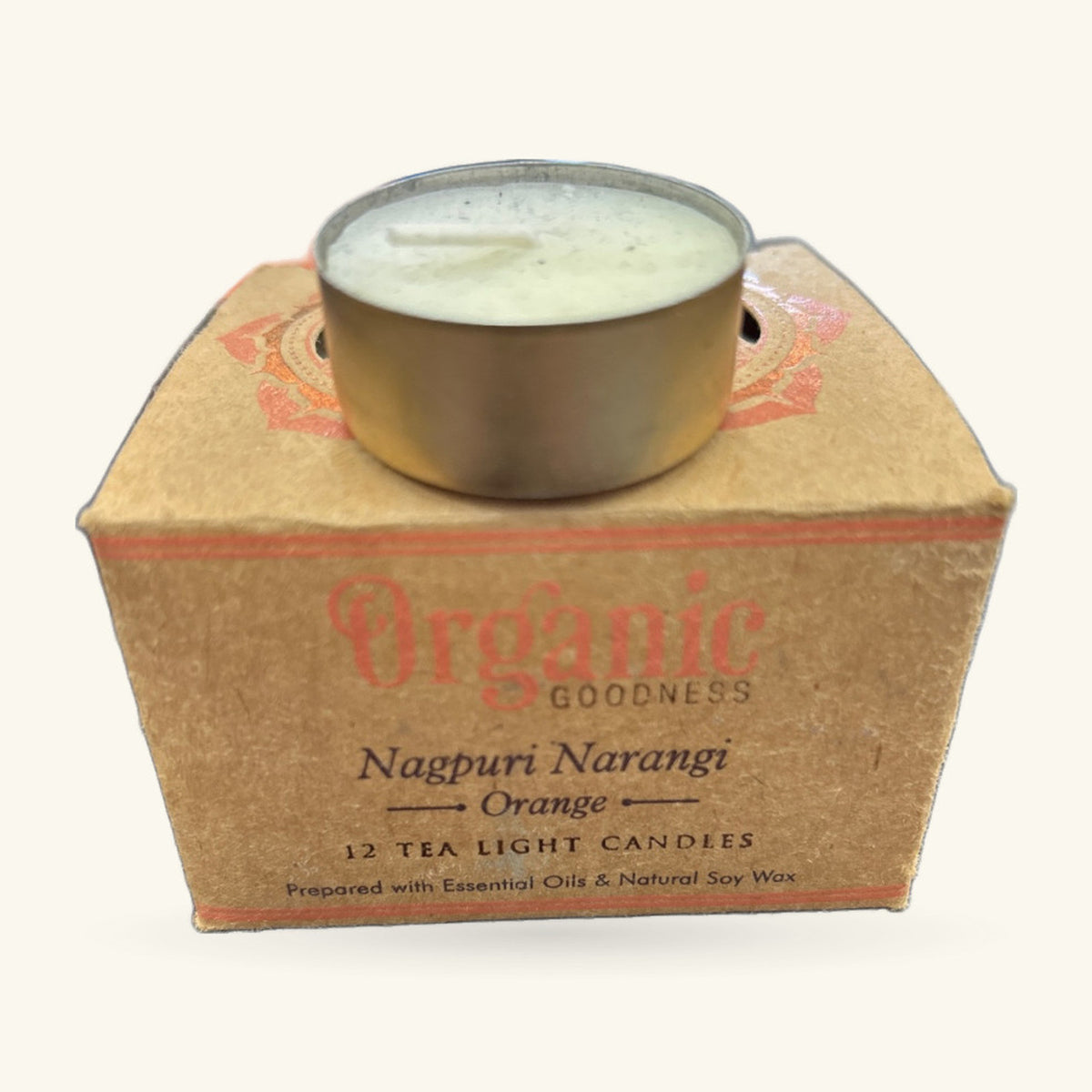 Cream tea light candle in metal holder on cardboard box labelled Organic Goodness Nagpuri Narangi Orange