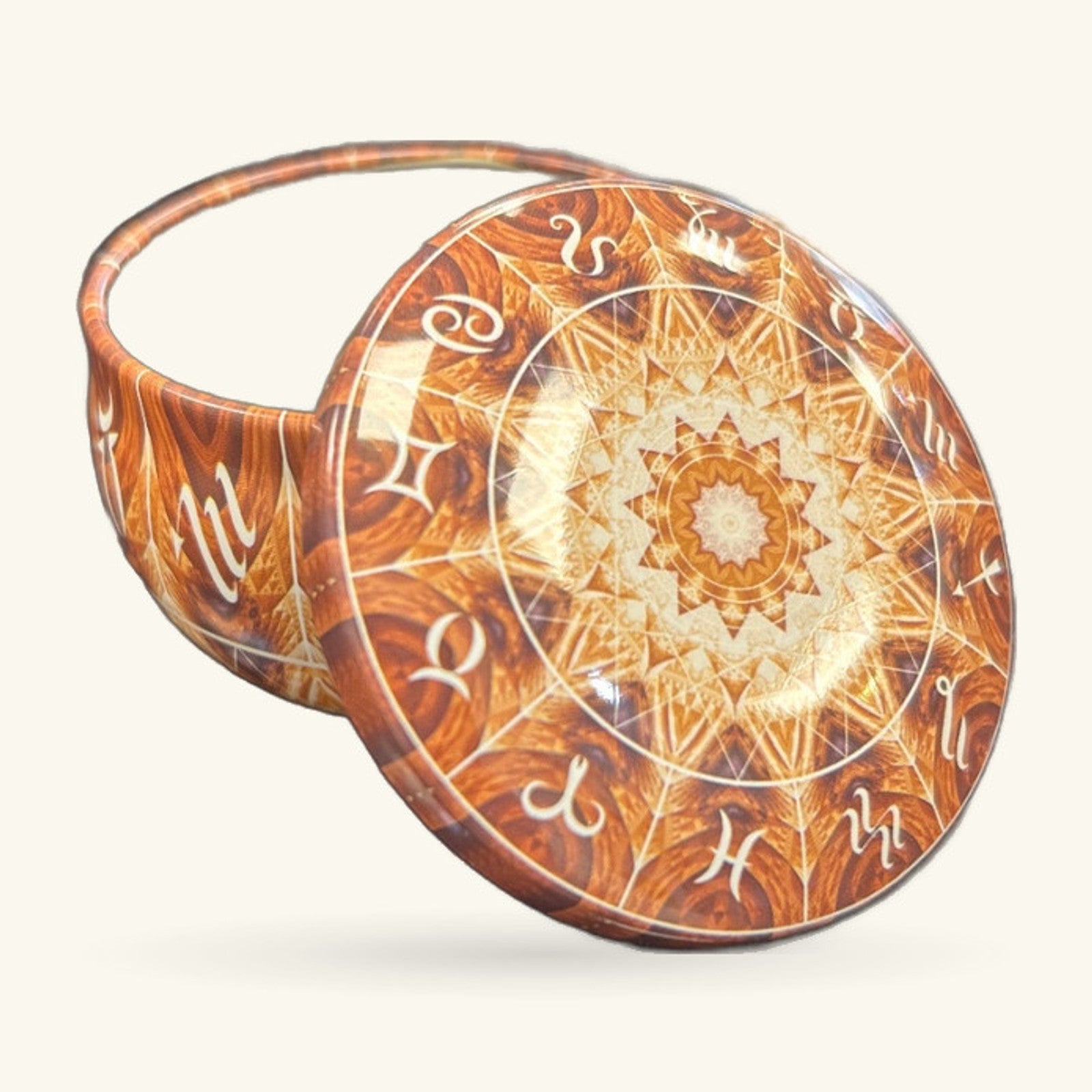 Circular zodiac tin with warm brown and cream enamel decoration, lid propped open