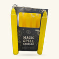 Two bright yellow spell candles in a black box labeled 'Magic Spell Candles Success' with mystical gold foil designs