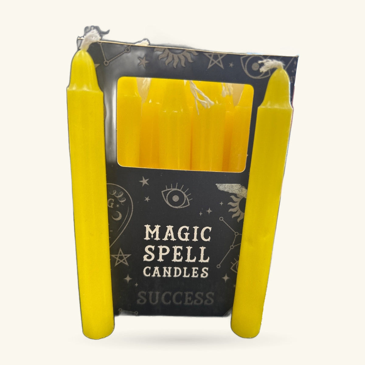 Two bright yellow spell candles in a black box labeled 'Magic Spell Candles Success' with mystical gold foil designs