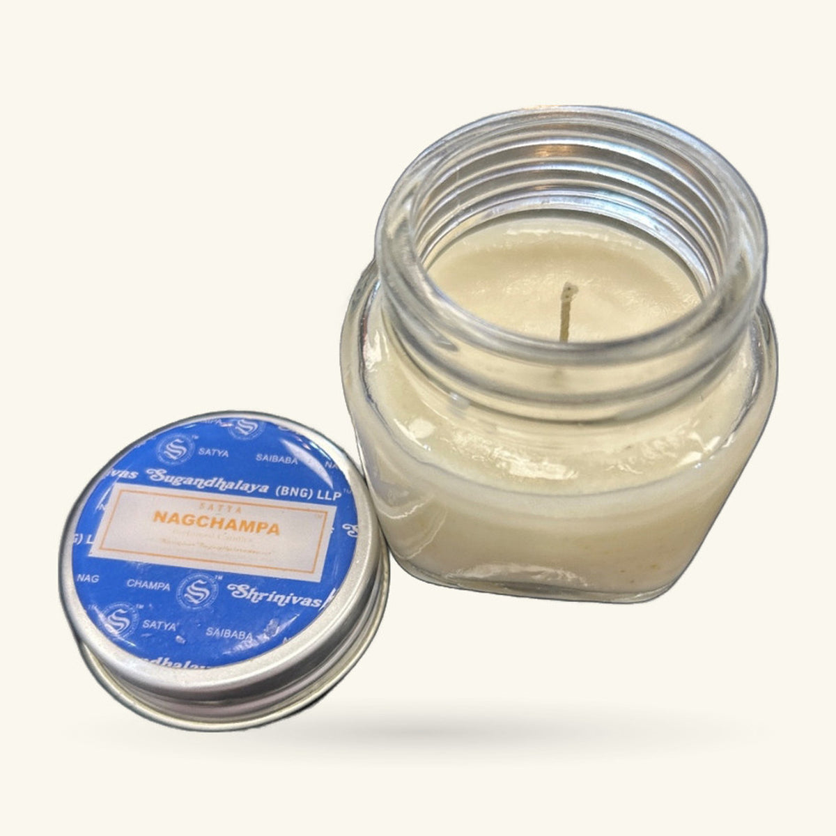 Satya Nag Champa jar candle with blue Saibaba label, cream-coloured wax and wick visible, lid shown separately