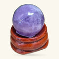 Purple amethyst sphere nestled in a curved wooden stand against a cream background.