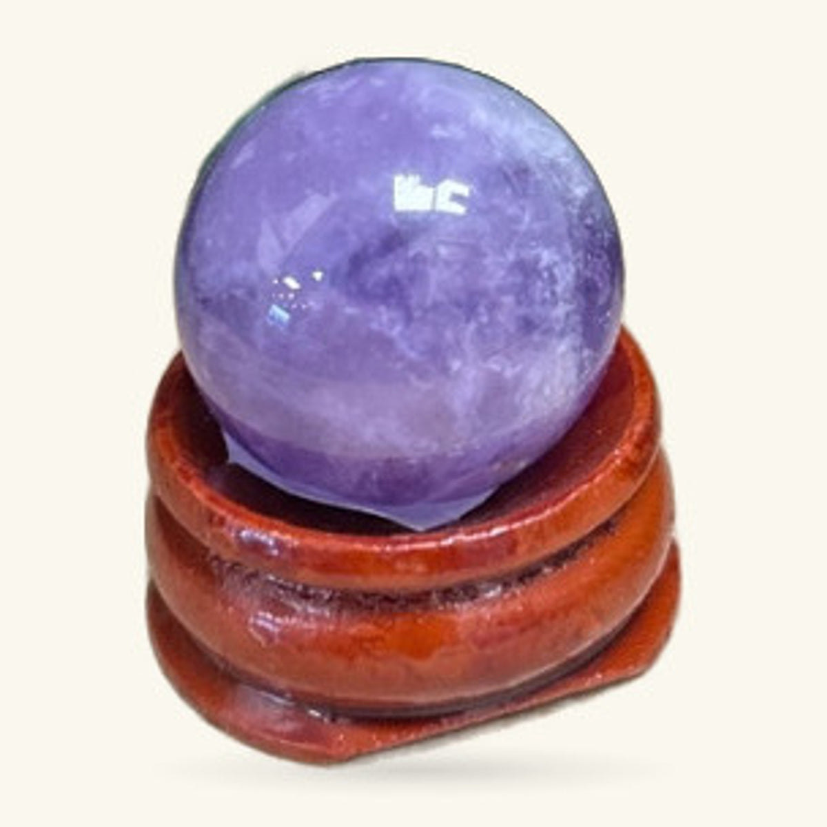 Purple amethyst sphere nestled in a curved wooden stand against a cream background.