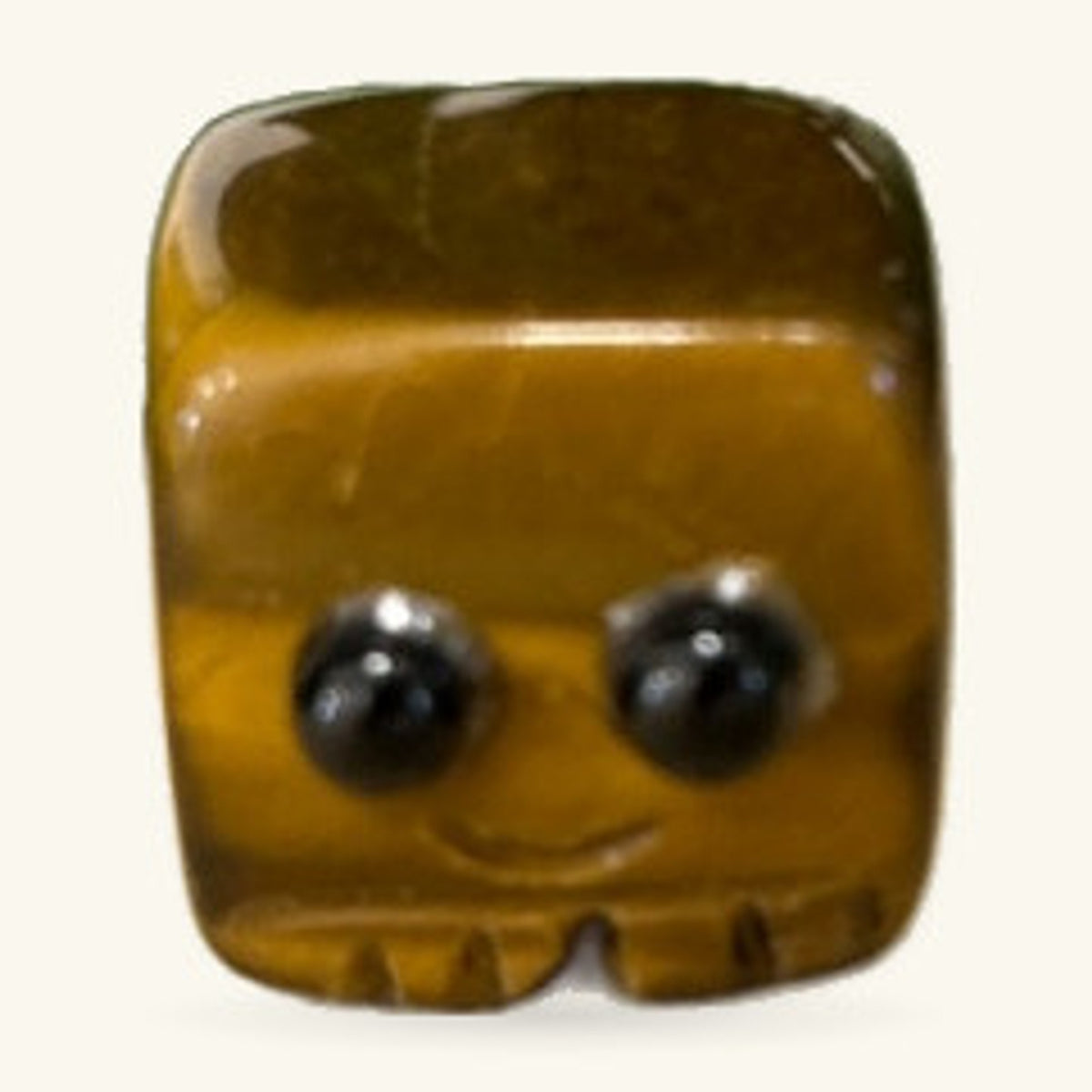 Golden-brown tigers eye stone carved into a rounded block buddy with a smiling face and two black eyes