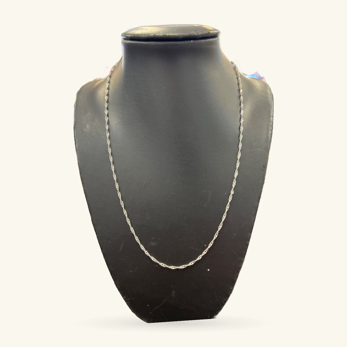 Silver chain necklace draped on a black neck display form, shown against a light background.