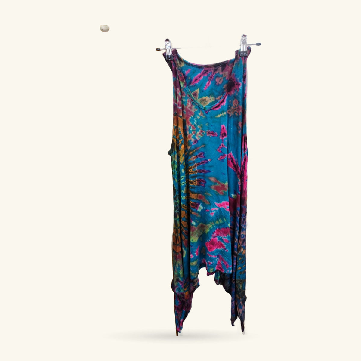 Tie dye tank dress in turquoise, magenta, and gold, hung on wooden pegs against a cream wall.