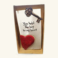 Wooden plaque with white panel, ornate bronze key, red textured heart, and black text reading 'You hold the key to my heart'