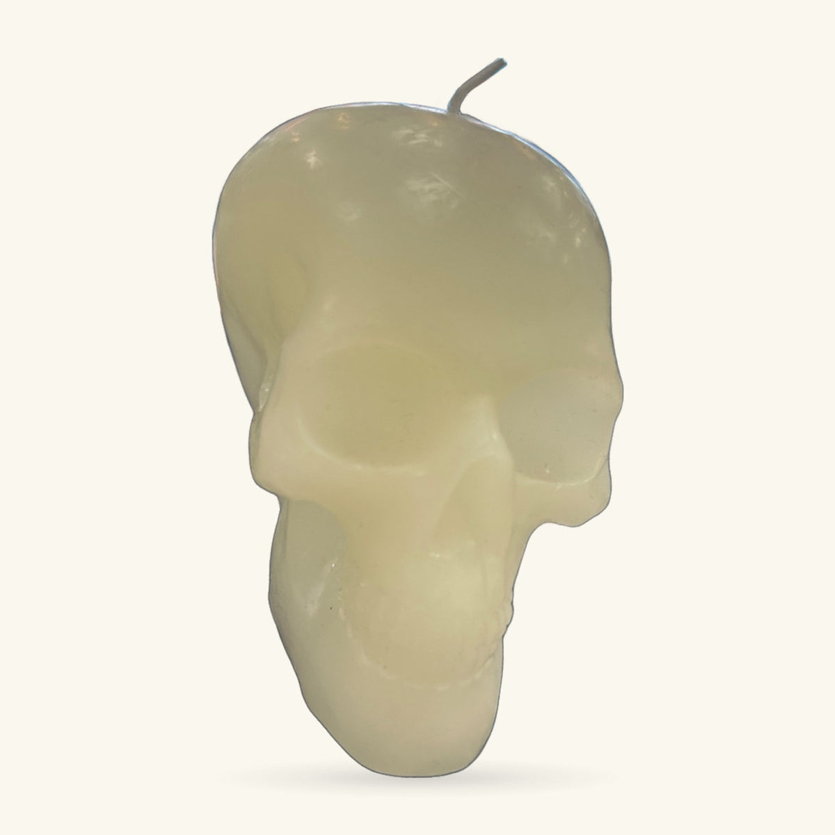 Cream-coloured skull-shaped candle with a grey stem, shown against a light background.