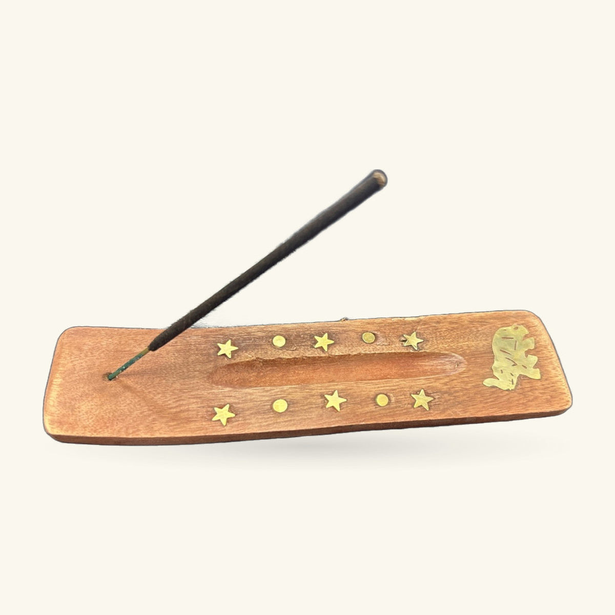 Wooden incense holder with brass stars and circles, black incense stick resting in groove