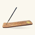 Wooden incense holder with brass sun and stars, black incense stick resting in groove