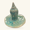 Blue-green ceramic Buddha head incense holder with a round dish base and pointed ushnisha crown