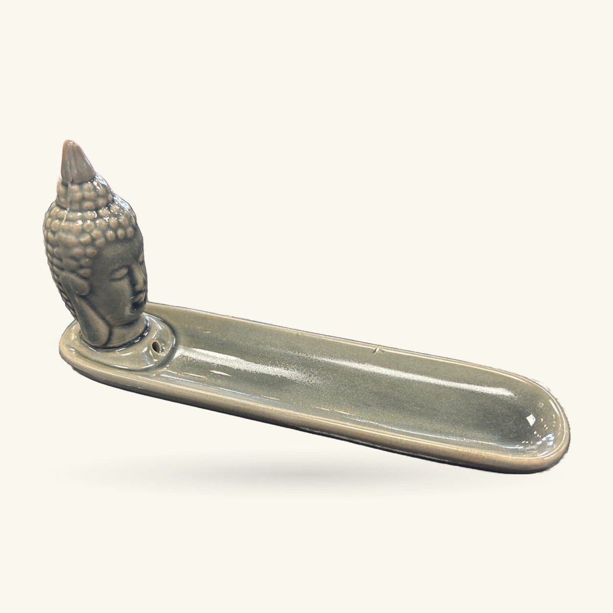 Black ceramic Buddha head incense holder with elongated dish base, side view on neutral background