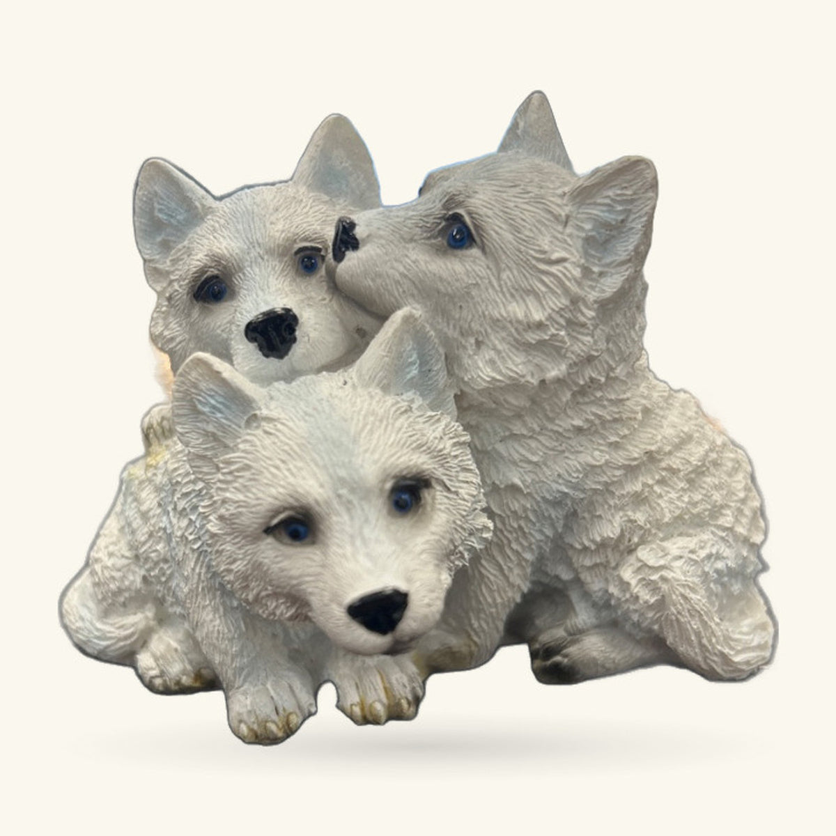 Three white ceramic wolf pup figurines huddled together, with black noses and blue eyes.