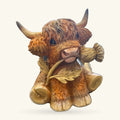 Highland cow ornament with long curved horns, brown and cream fur, holding a golden thistle, seated pose