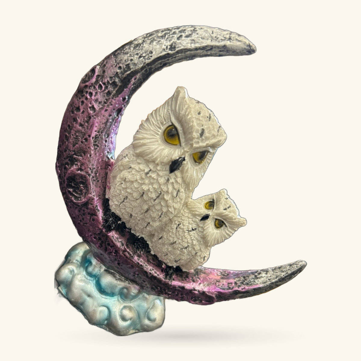 Two cream-coloured owls perched on a crescent moon ornament with purple and grey glaze, seated on a decorative blue-grey base.