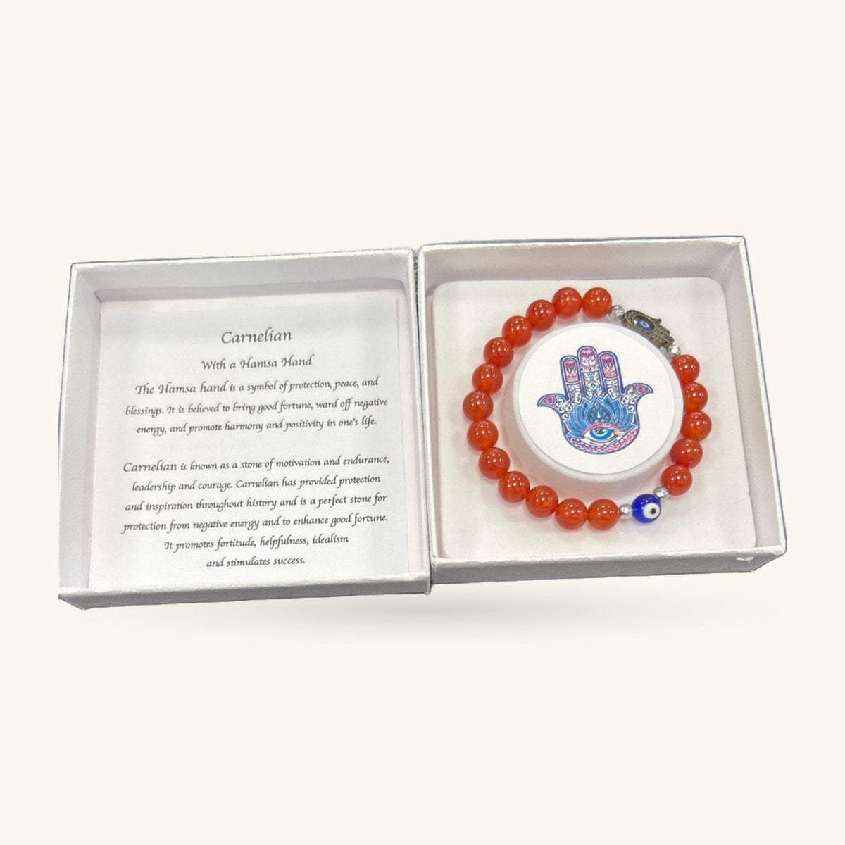 Hamsa Evil Eye Carnelian Bracelet with red-orange beads, blue enamel eye bead, and Hamsa charm, displayed in open white gift box with information card