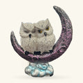 White owl perched on a crescent moon in purple and grey, sitting on a pale blue cloud base.